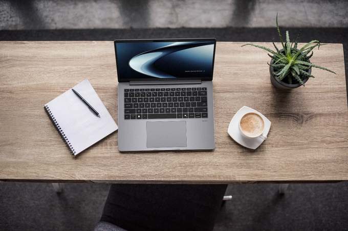 ASUS ExpertBook P5 G2 di atas meja kerja kayu, ditemani kopi dan tanaman kecil